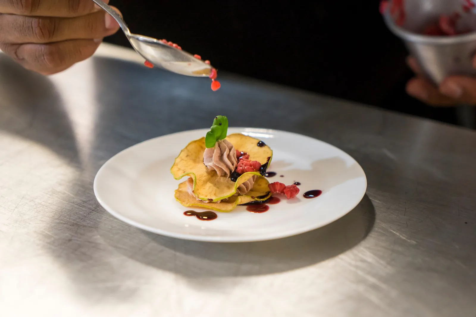A pastry chef garnishing an elegant dessert with berry sauce