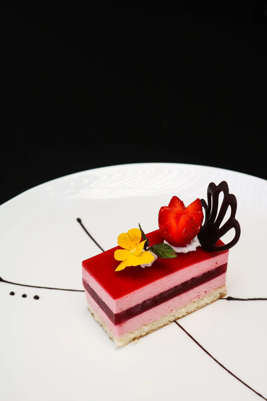 Raspberry mousse cake with vibrant garnishes on a white plate