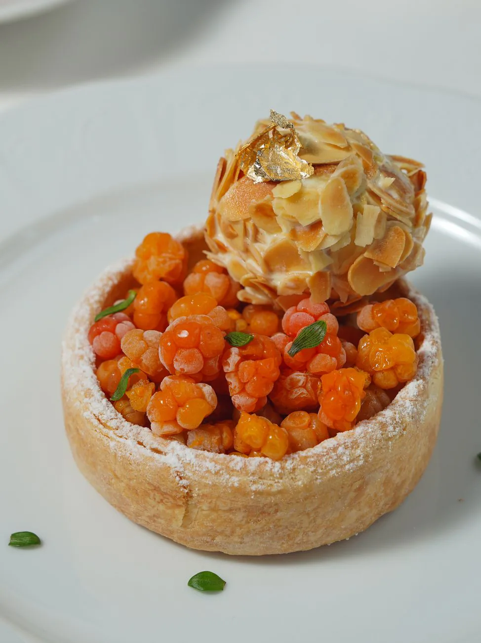 A cloudberry tart topped with almond-caramel swirl and gold leaf