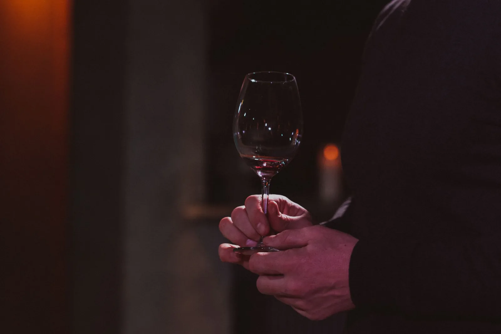 Hands raising a glass of red wine in a dimly lit room