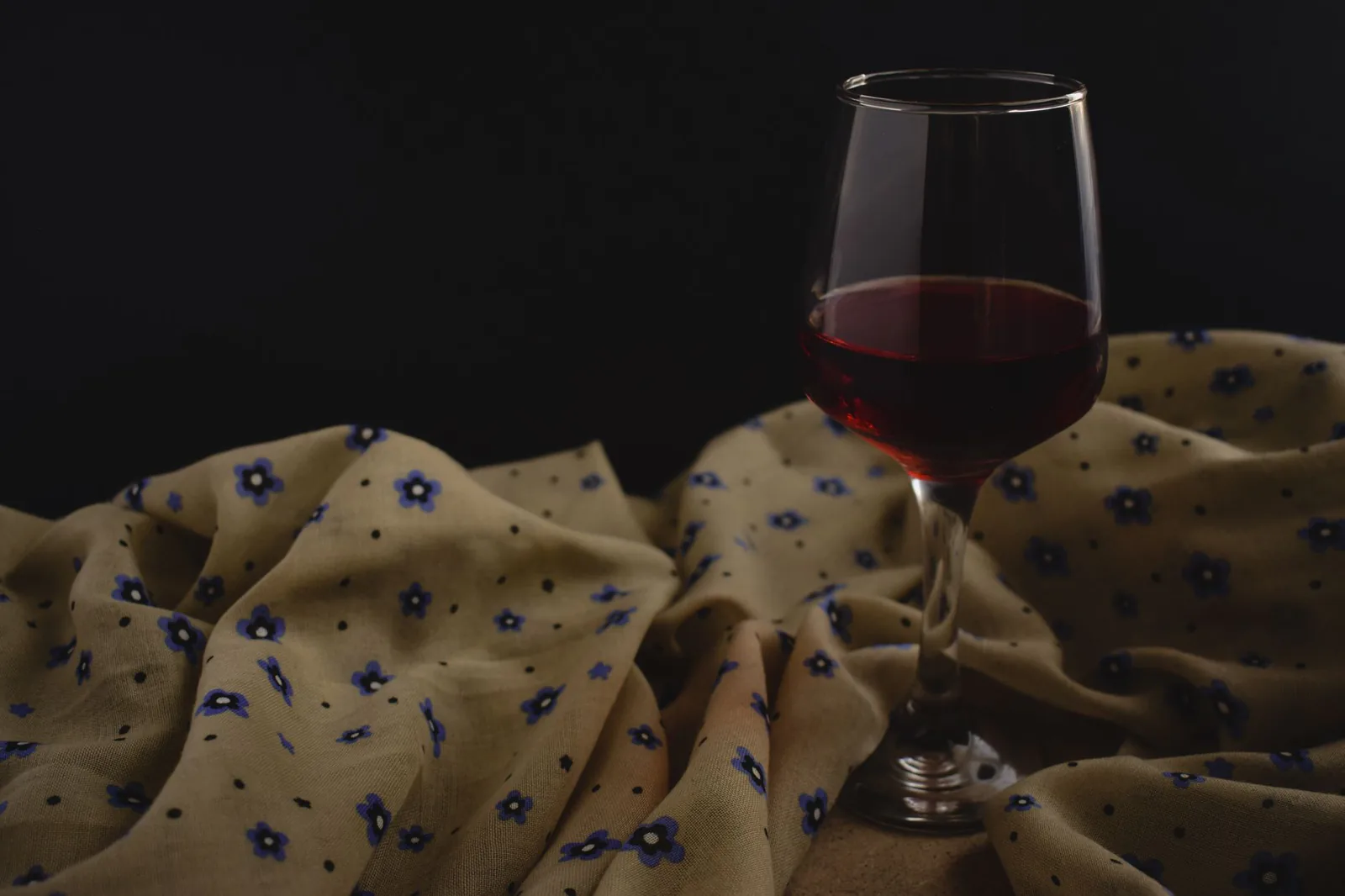 A glass of red wine beside flowers against a dark background